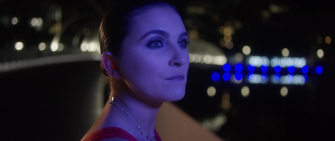 A woman by a coast with water and lights in the background
