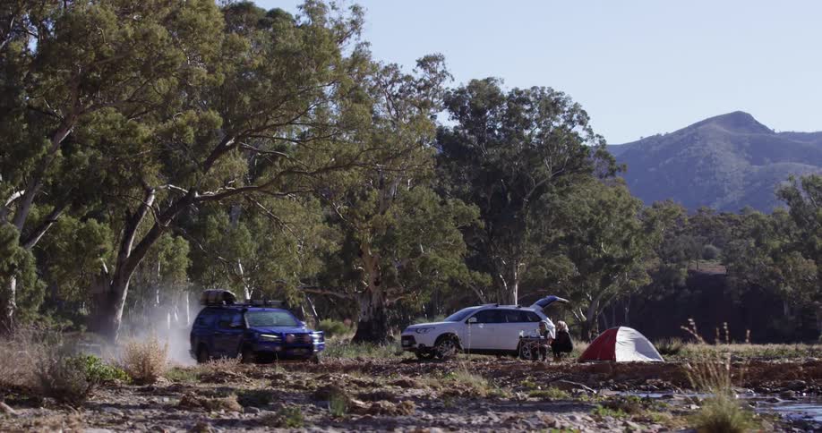 A couple sits at a table near their tent and truck as an suv travels past splashing water