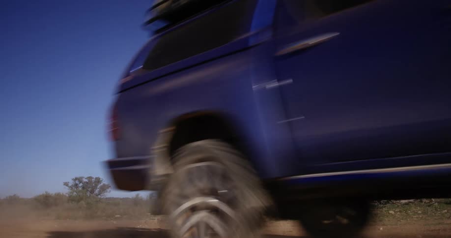 A vehicle travels around a dirt road past a tin weather vane on a clear day