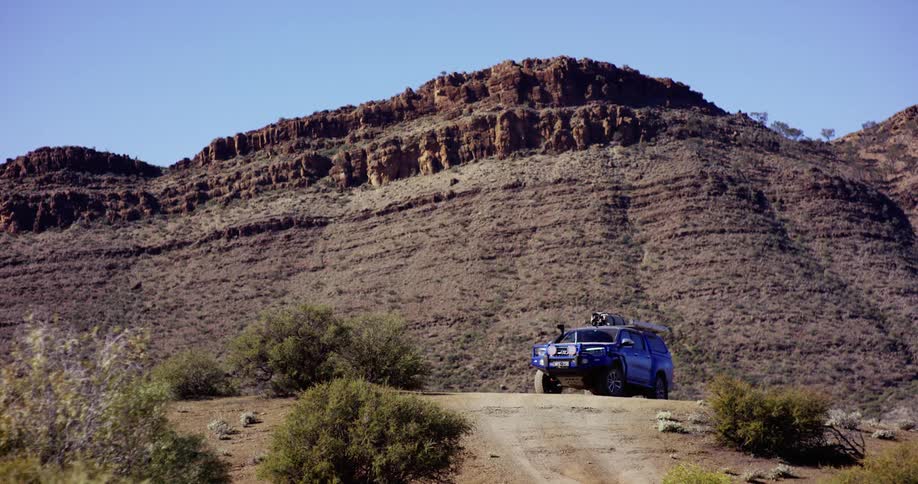 A vehicle driving on a dirt road with a cliff and the sky in the background