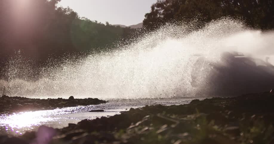 Water splashes as a sport utility vehicle drives through a creek and river near a forest