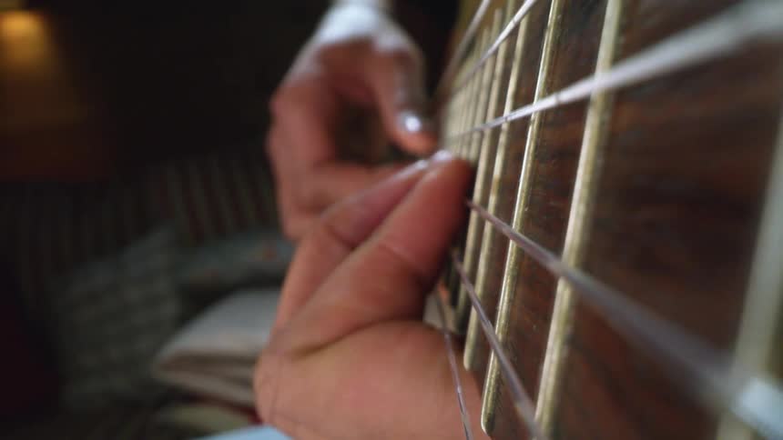 Fingers moving along the neck of a guitar plucking strings as a man plays