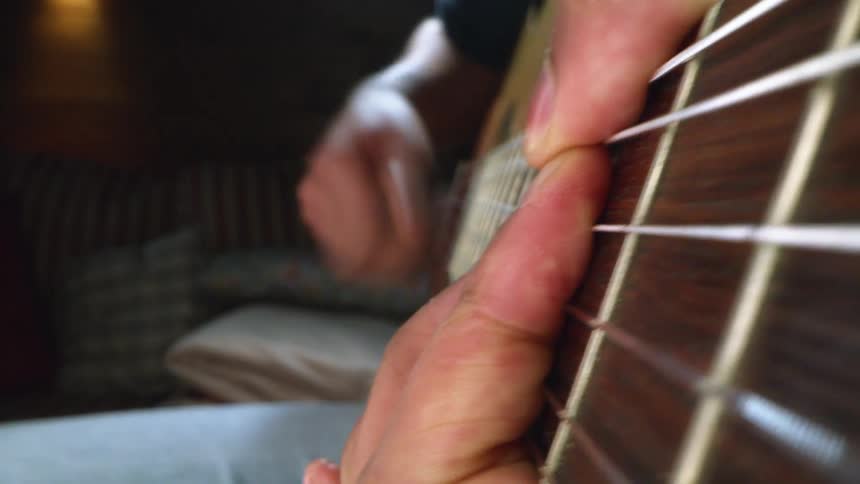 Guitarist is playing an acoustic guitar with one hand grasping the neck and moving his fingers across the frets as he strums the strings with his other hand