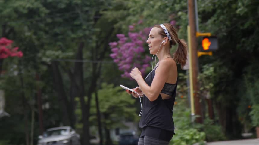 Woman jogger coming to a stop at an intersection in an urban area