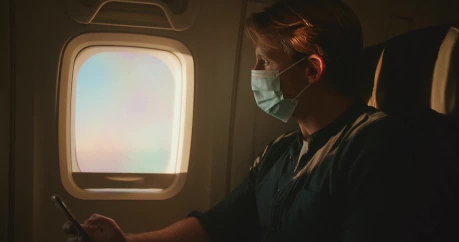 A man sits on an airplane looking at his phone then looks out the window