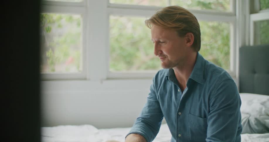 Man sitting on bed near windows talks via video call on laptop