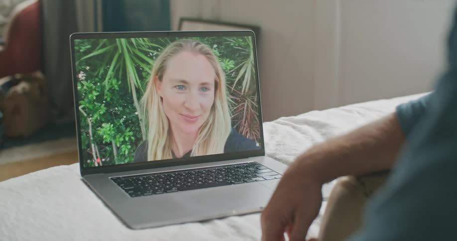 Man sitting on bed talks via laptop with woman standing outdoors