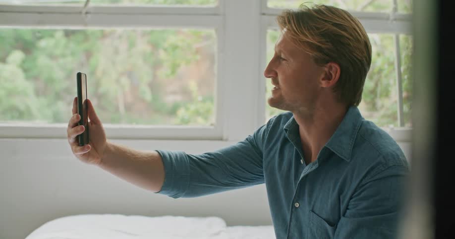 White man next to a big window on a video call on his smartphone