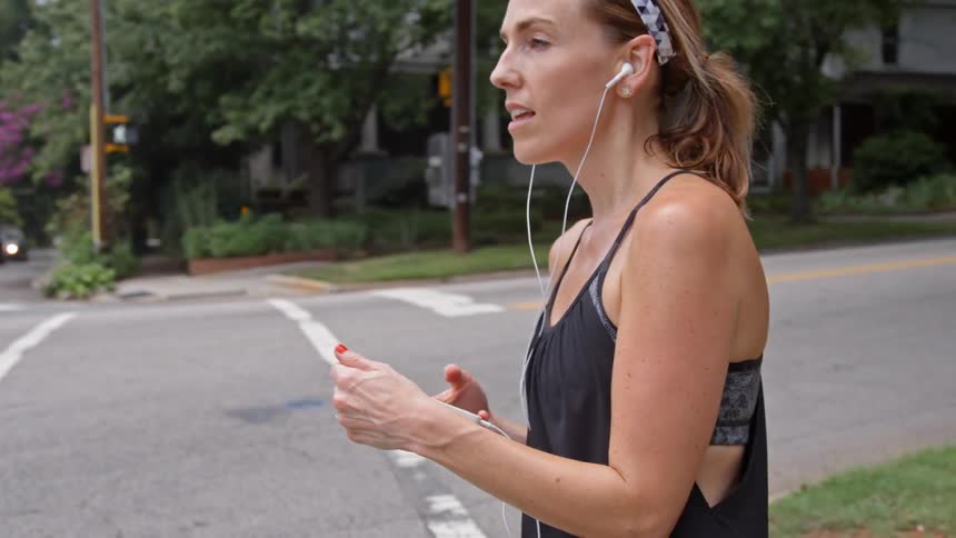 A woman jogs then stops to look at her phone at the corner