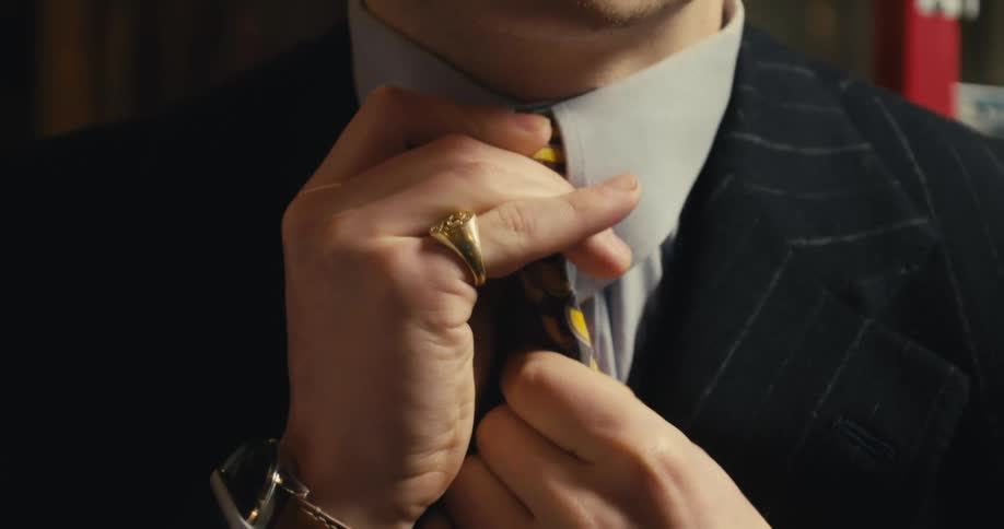 A man wearing a gold pinky ring and a pin striped suite adjusts his tie