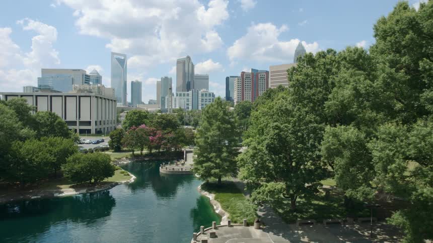 A river surrounded by trees with a city skyline the sky and clouds in the background