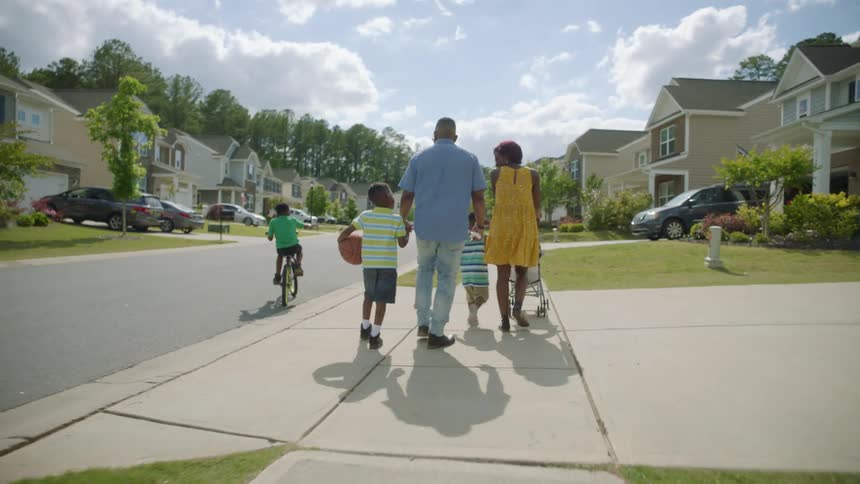 A family walking on a residential sidewalk on a sunny summer day