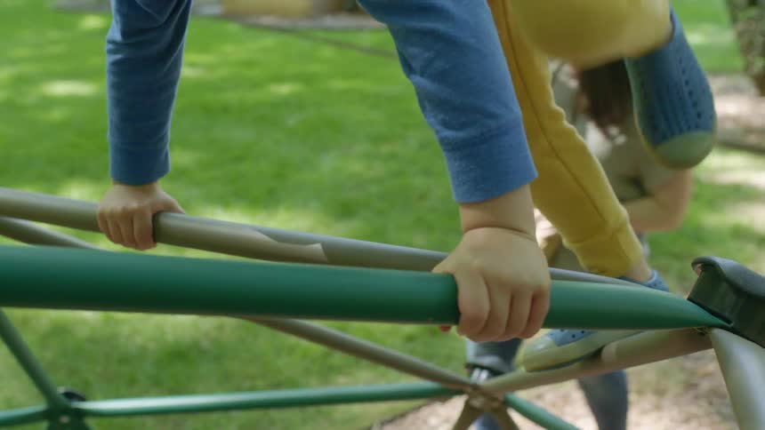 Young boy climbing over a dome climber in a playground while his mother watches
