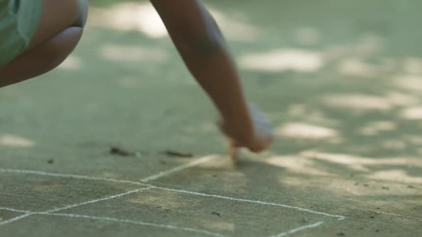 A child drawing hopscotch squares on a sidewalk with chalk