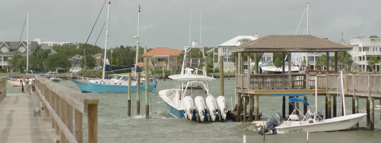 Small boats bob in the water as they are parked in a marina near a neighborhood