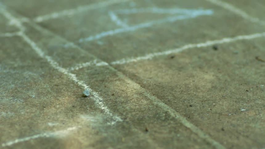 Hopscotch sits drawn in chalk near pebbles on smooth concrete