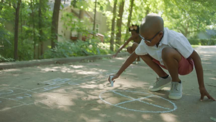 A brother and sister draw on their driveway in blue chalk
