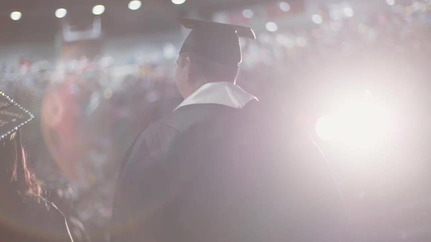 Graduates are walking into a stadium with people watching
