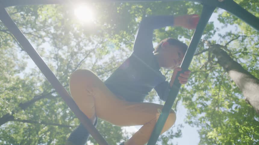 Sunlight over a boy playing on an outdoor dome climber under the trees