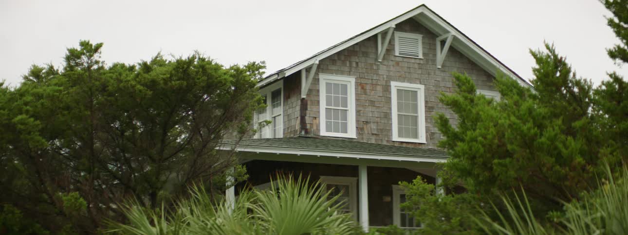 Trees and bushes surround grey two story house with white trim