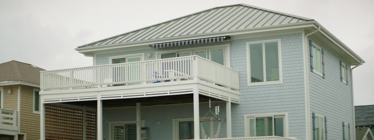 A blue house with a large white deck and metal roof