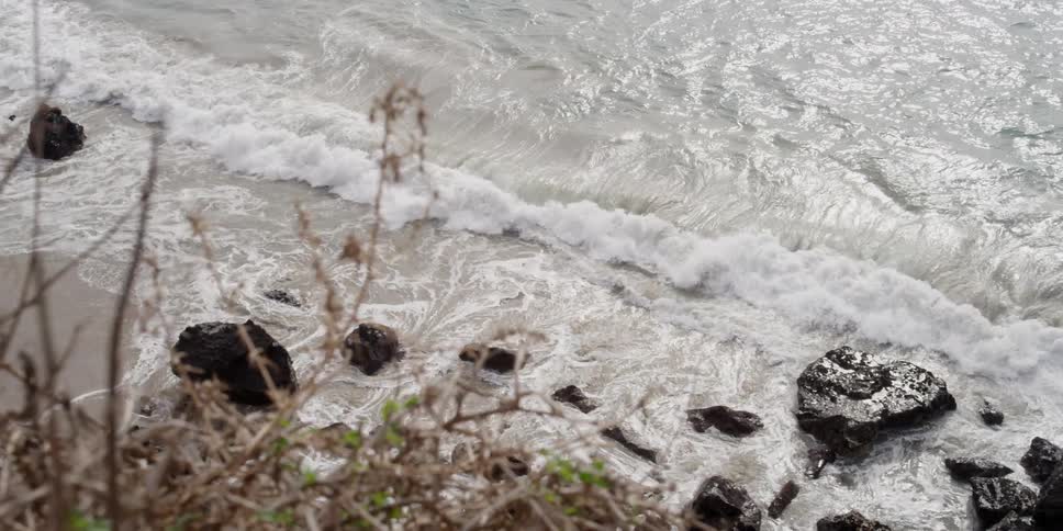 Waves crash on a shore below a cliff