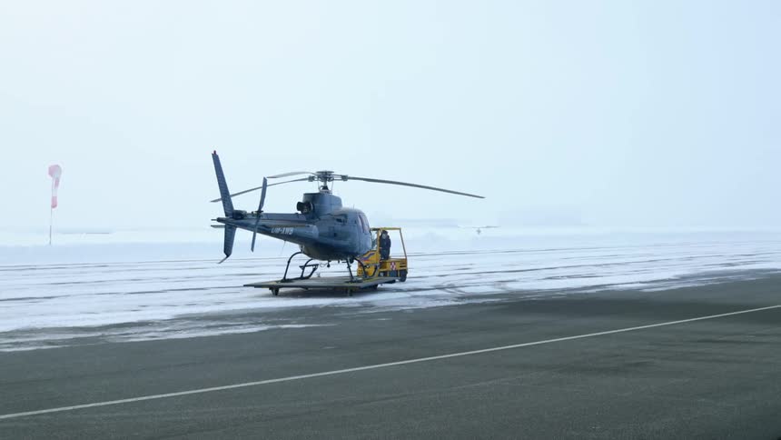 Operator pulling a helicopter over a cart through the snow covered runway