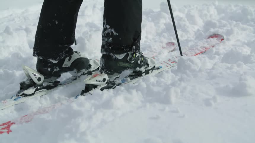 A person putting on skis in the snow with trees in the background
