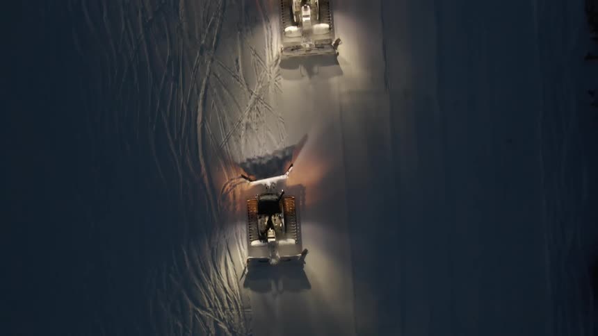 Aerial view of snow plows driving down a snow covered road at night