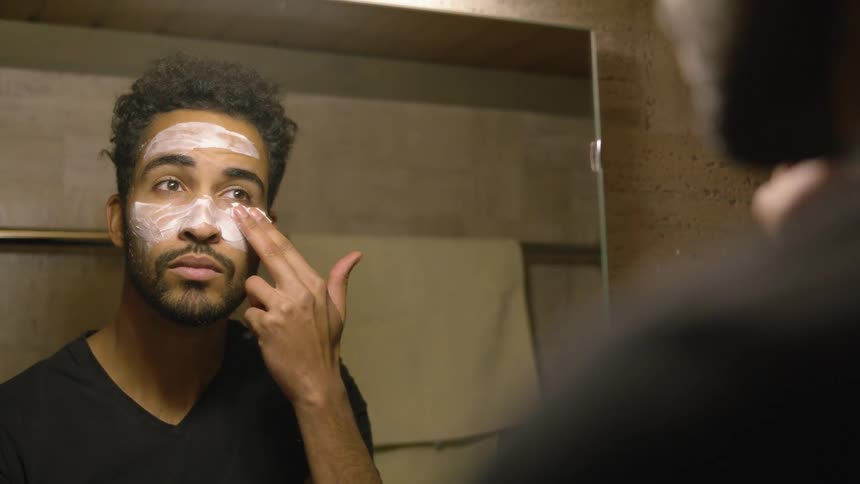 A man applying face cream while looking in a bathroom mirror