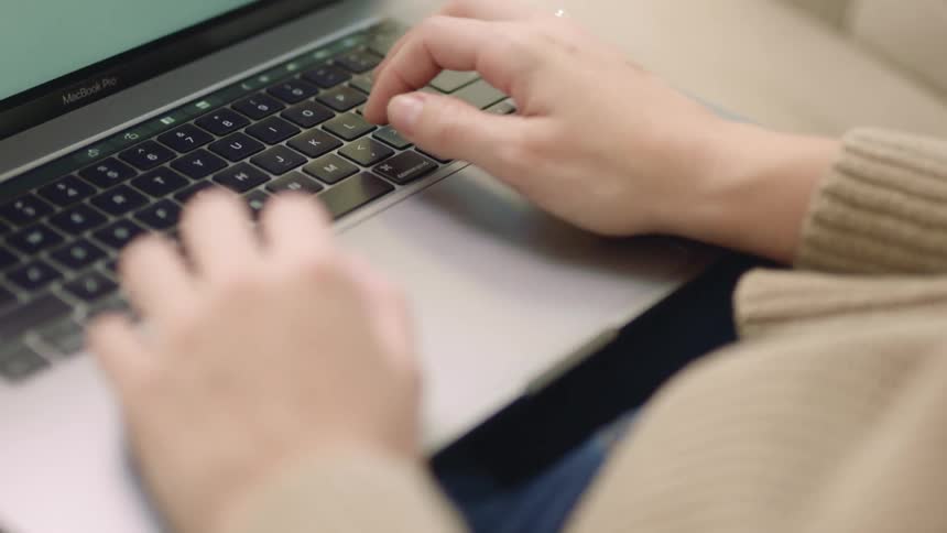 A person working from home is sitting and typing on their laptop