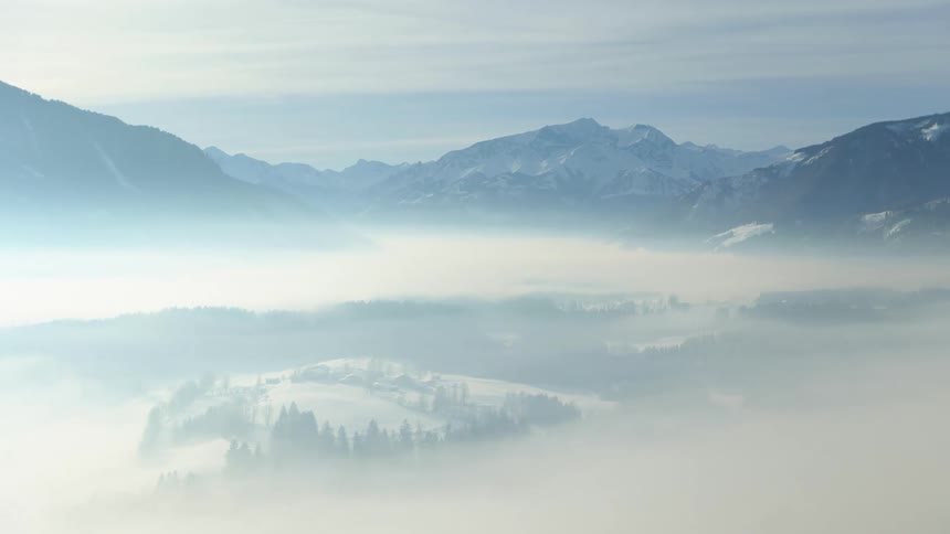 Aerial view of white fog over the pine tree forests in the snow covered mountains