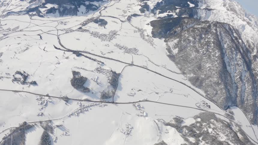 Person wearing a wing suit is gliding over a snow covered mountain canyon