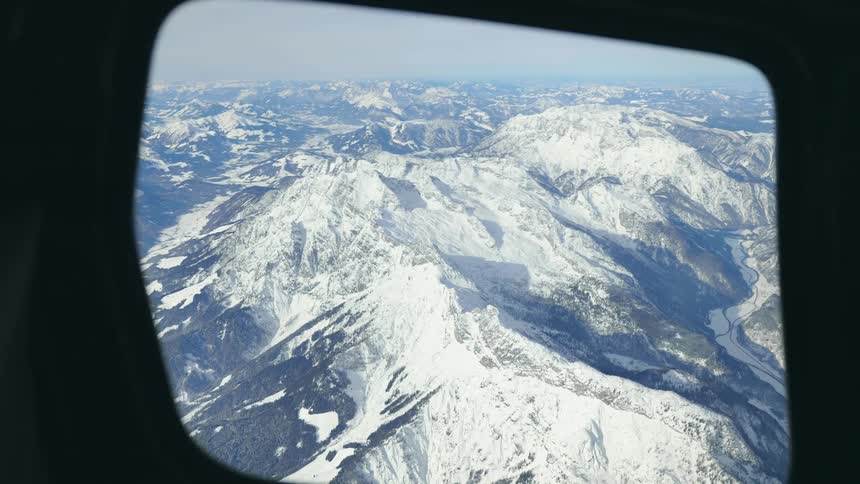 A view of snowy mountains on a winter day from an airplane window
