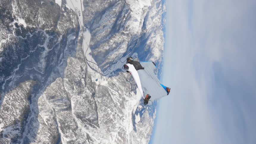 Skydiver wearing a wing suit is floating and gliding over snow covered mountains