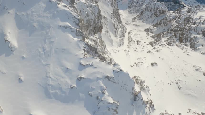 A person glides over a snowy mountain top in a parachute like gliding suite during the day