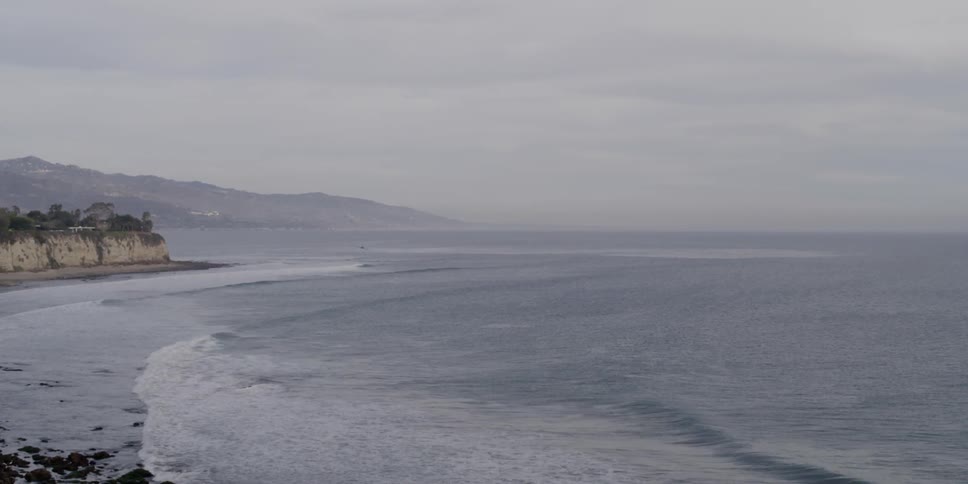 Two planes fly past a beach with rocks and cliffs on an overcast day