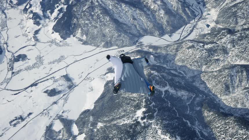 Skydiver wearing a wing suit is gliding over snow covered mountains