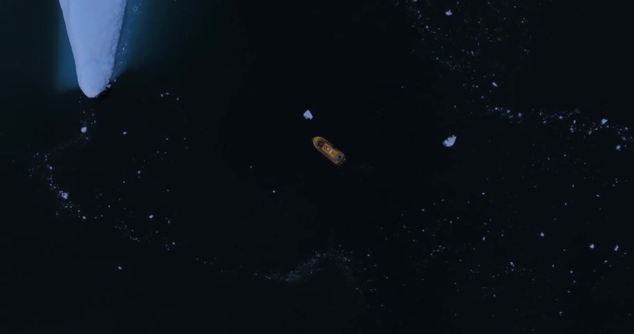 A birds eye view of a boat floating in arctic waters near icebergs