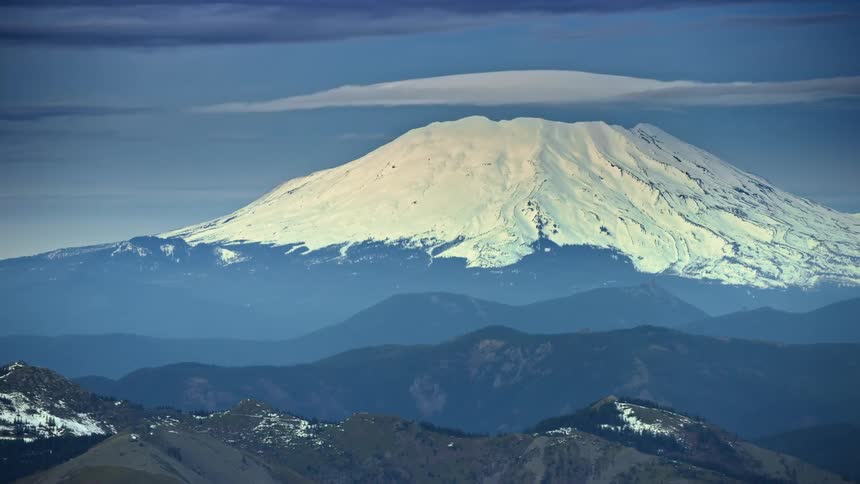 A stormy winter aerial of Mount St Helens in winter with a large lenticular cloud forming above the mountain as seen from a big airplane
