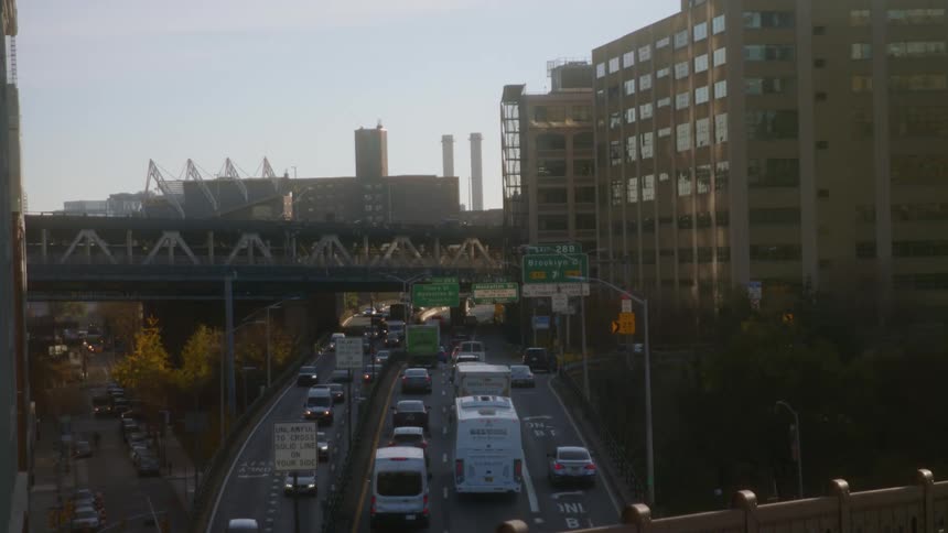 Cars travel on a highway in an urban city with buildings around it and people walking by down below