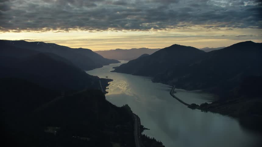 Aerial of the Columbia River Gorge near Hood River Oregon at sunset with golden light pouring into the sky as the camera flies towards Portland