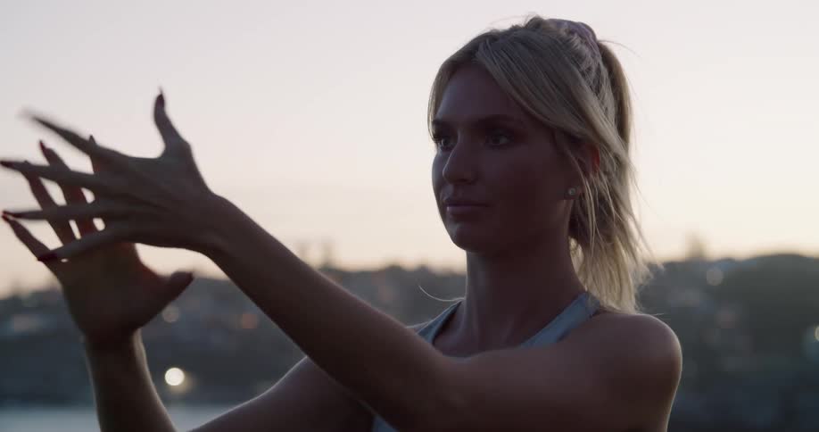 A woman stretches her hands preparing for exercise while outside at sunrise