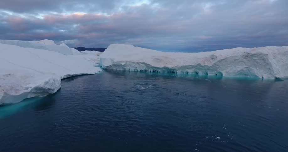A whale swimming in the ocean with glaciers the sky and clouds in the background