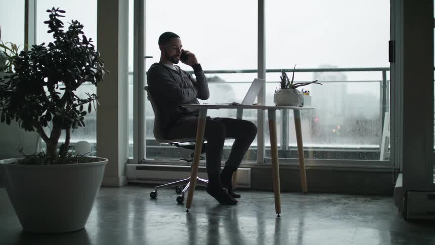 Man sitting near a large window indoors talking on a cell phone