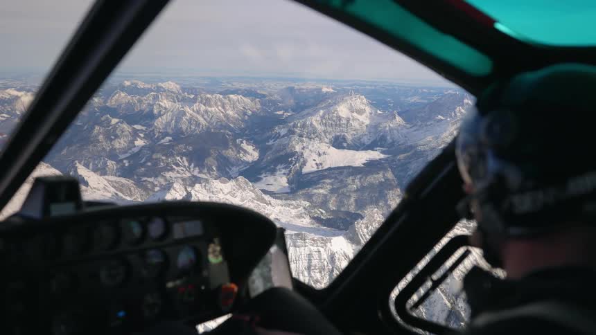 A pilot flying a helicopter over snowy mountains on a winter day