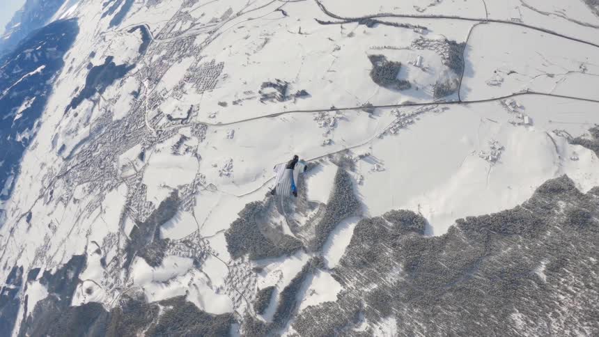 Aerial footage of a skydiver wearing a wingsuit falling over the snow covered peaks of a mountain range