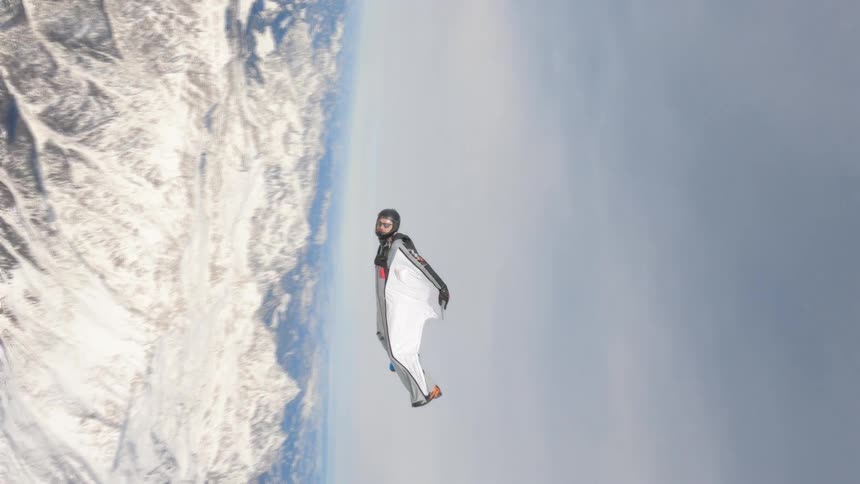 A person with a helmet skydiving with a mountain range the sky and clouds in the background