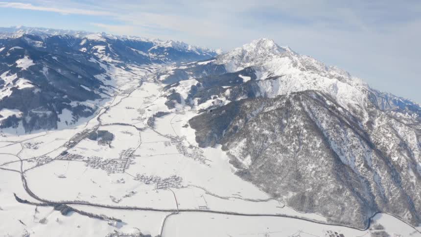 Skydiver opens parachute and glides over snow covered mountains on a cloudy day