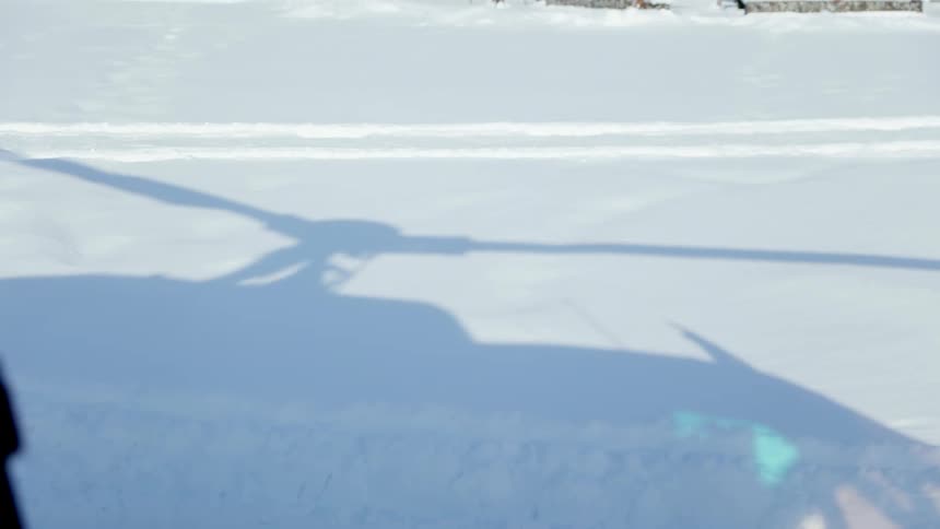 The shadow of the slowly decelerating rotors of a helicopter on the snow